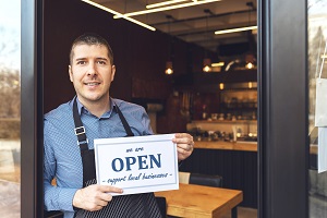 restaurant owner standing in doorway holding open sign