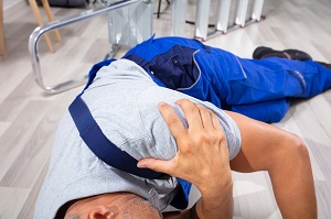 male worker laying on ground holding his shoulder in pain